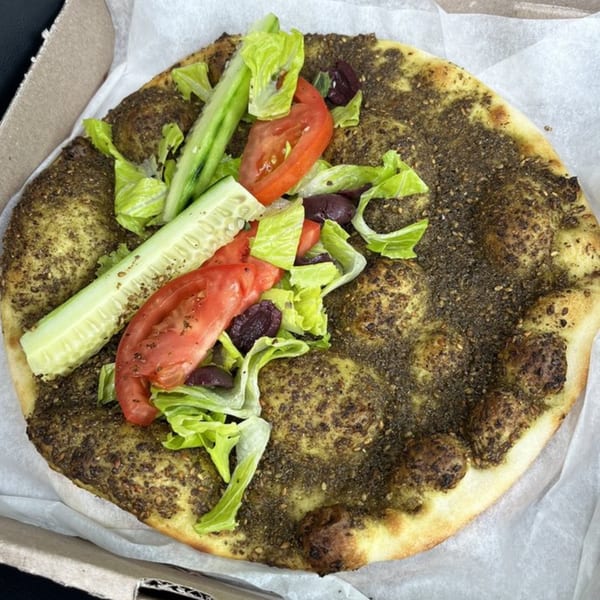Mediterranean za'atar flatbread topped with fresh lettuce, sliced tomatoes, cucumbers, and olives.