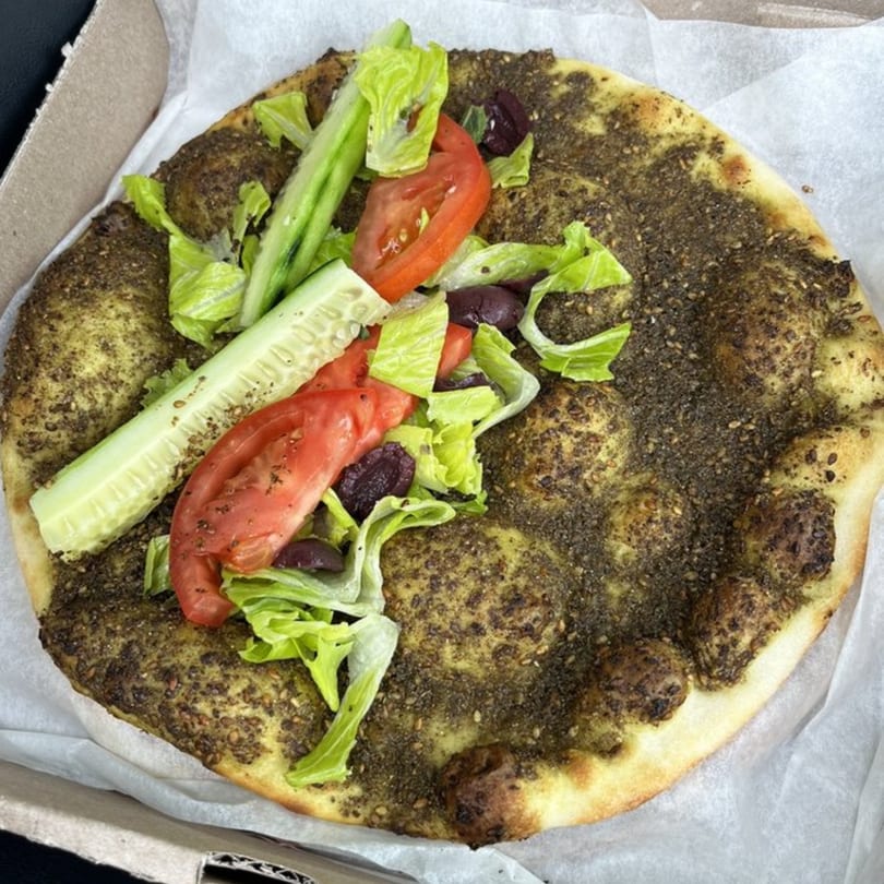 Mediterranean za'atar flatbread topped with fresh lettuce, sliced tomatoes, cucumbers, and olives.