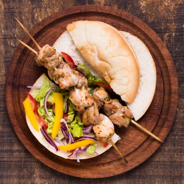 Mediterranean chicken shish kebab with fresh salad and bread on a wooden platter.