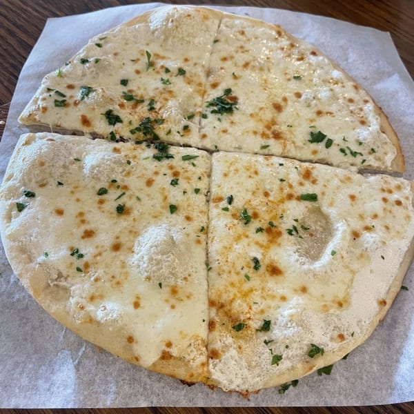 A round, flat Mediterranean bread, topped with melted white cheese and green herbs, cut into four pieces.
