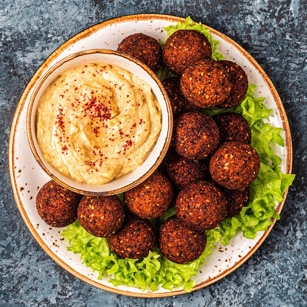 A plate of DoughLicious falafel with hummus and fresh lettuce on a dark background.