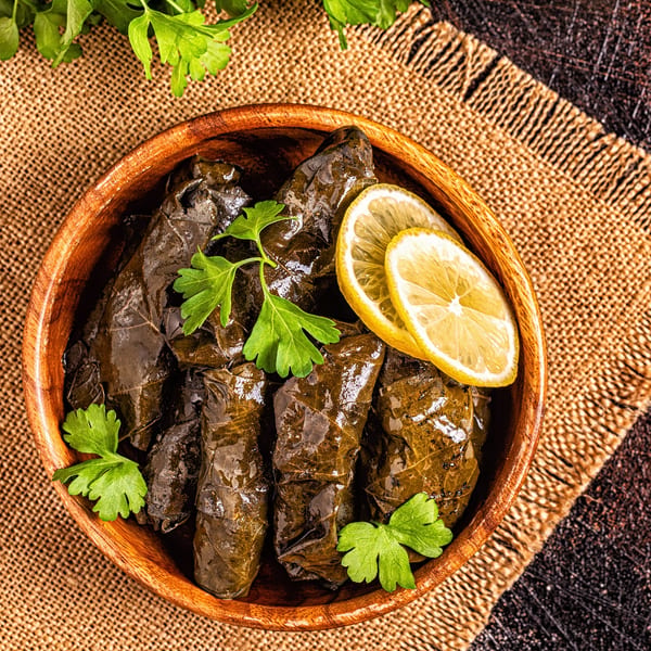 A wooden bowl of stuffed grape leaves (dolmades) garnished with fresh parsley and lemon slices.