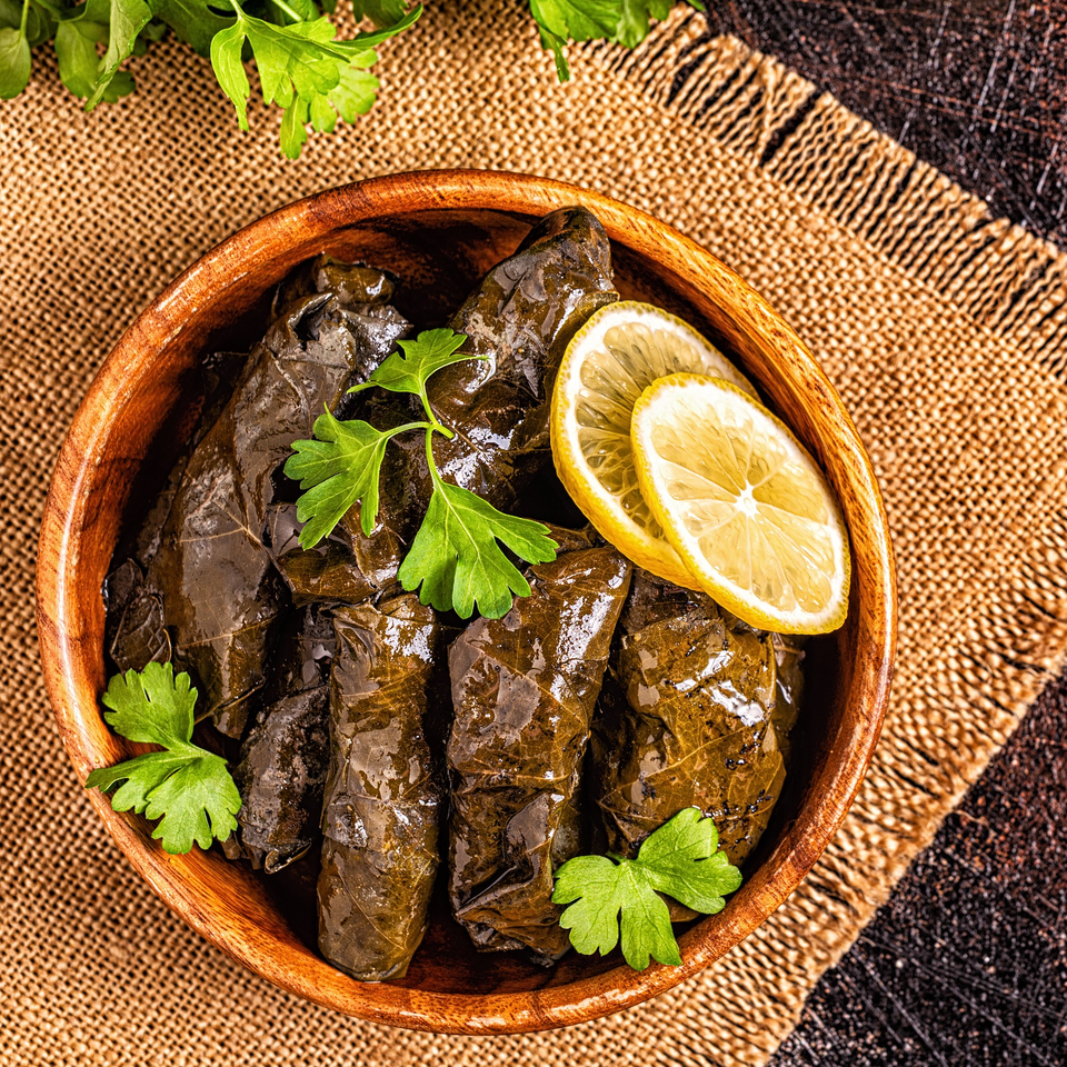 A wooden bowl of stuffed grape leaves (dolmades) garnished with fresh parsley and lemon slices.